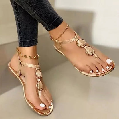 Women's gold flat sandals with three decorative circular metal buckles, worn with dark jeans and gold anklets