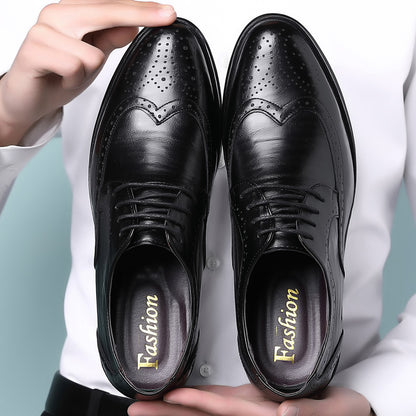 Pair of black leather men's dress shoes with brogue detailing and laces held by a person in white shirt