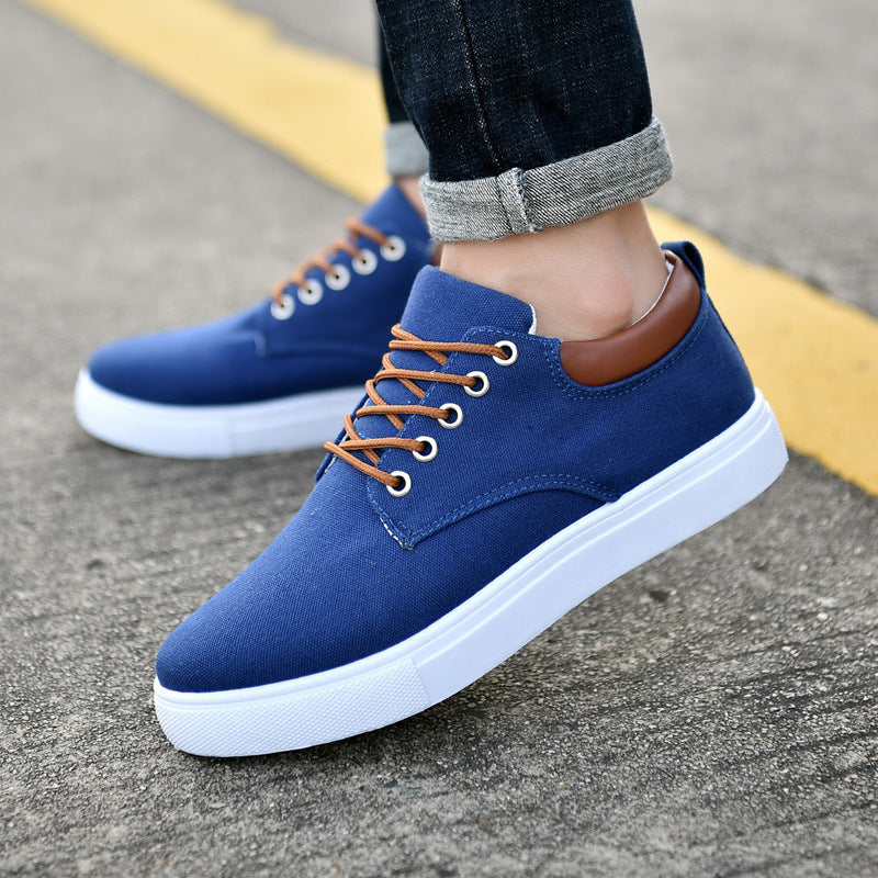 Blue men's canvas sneakers with white soles and brown laces worn with rolled-up dark jeans on pavement