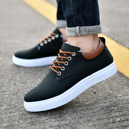 Black men's casual sneakers with brown laces and heel collar, white rubber sole, worn with cuffed jeans on asphalt