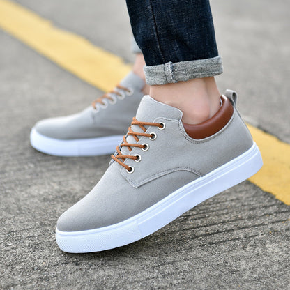 Men's grey canvas sneakers with brown laces and collar, white sole, worn with rolled dark jeans on pavement