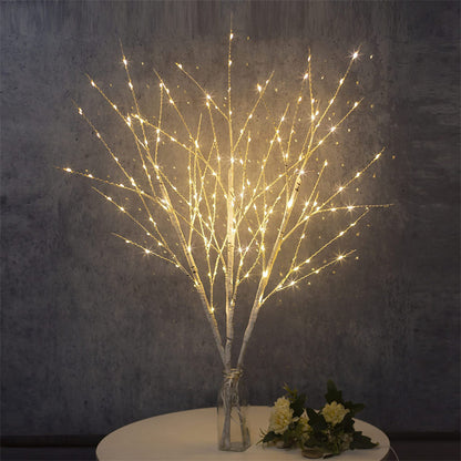 Decorative white birch branches with warm white LED lights arranged in a clear vase on a round table