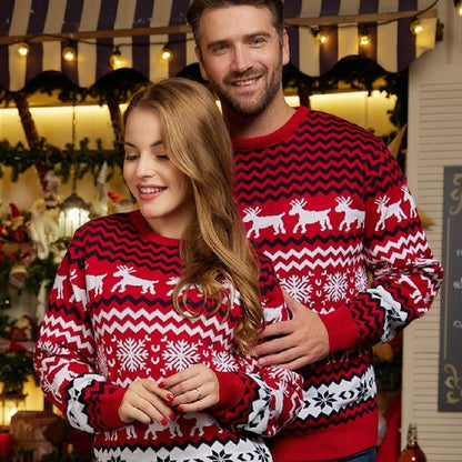Couple wearing matching red and white Christmas sweaters with reindeer and snowflake patterns in festive setting