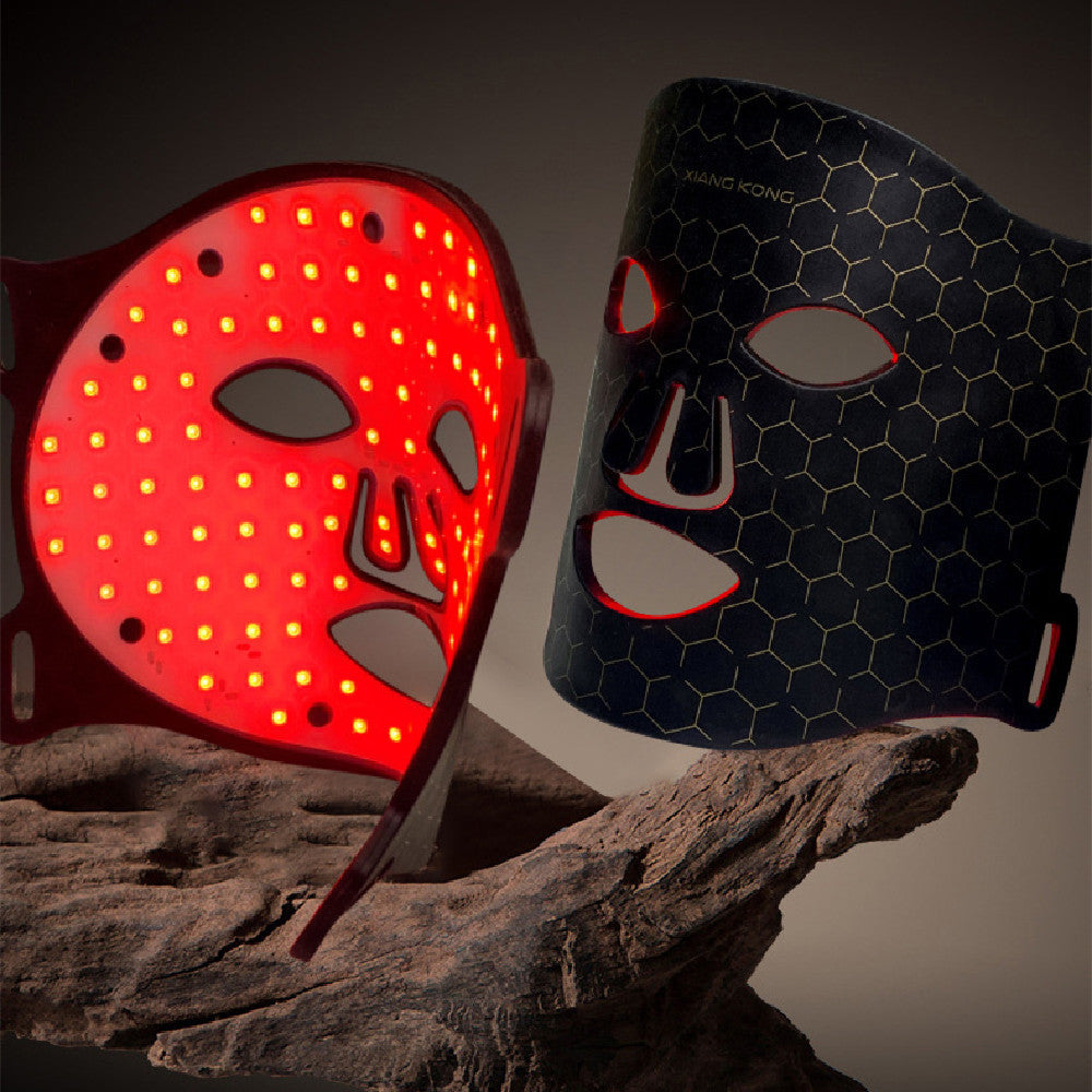 Portable black LED light therapy face mask with honeycomb pattern and red glowing lights for skin rejuvenation