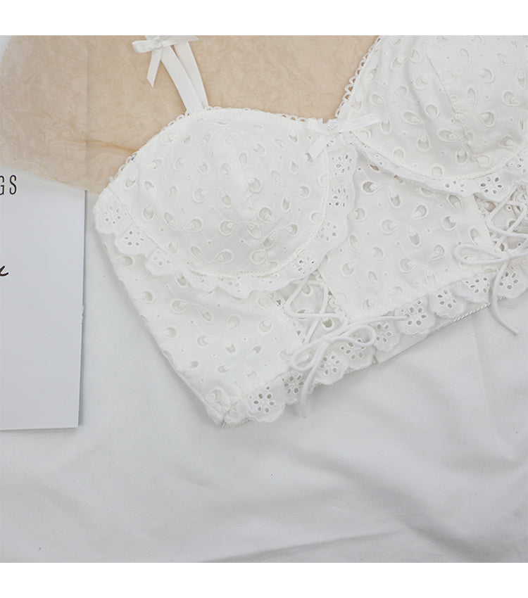 Close-up of white lace cotton bra with eyelet pattern and ribbon details on white fabric