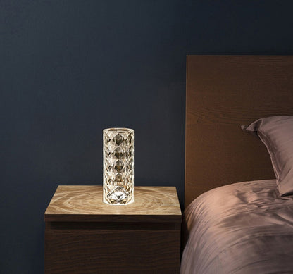 Modern crystal table lamp with a geometric pattern on wooden nightstand next to bed with brown bedding