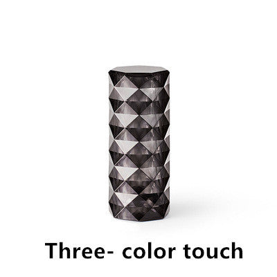 Black geometric faceted cylindrical lamp with three-color touch feature on white background