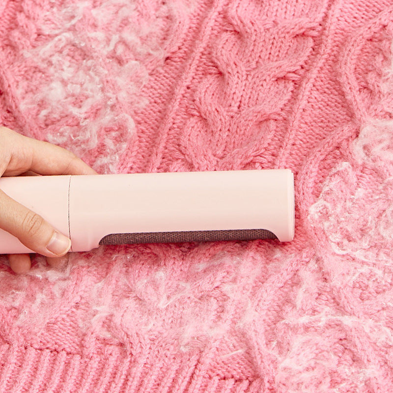 Hand using a pink self-cleaning pet hair remover brush on a pink knitted sweater with pet hair