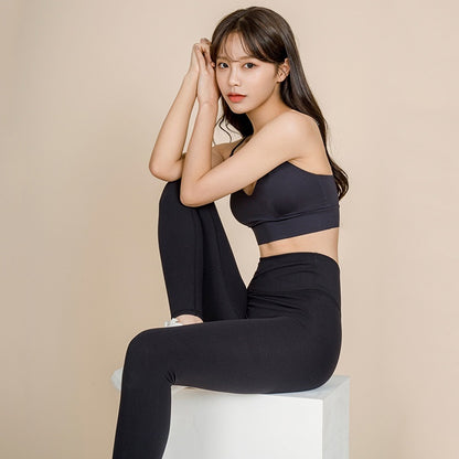 Woman wearing black sports bra and leggings in studio, posing seated for fitness activewear shoot