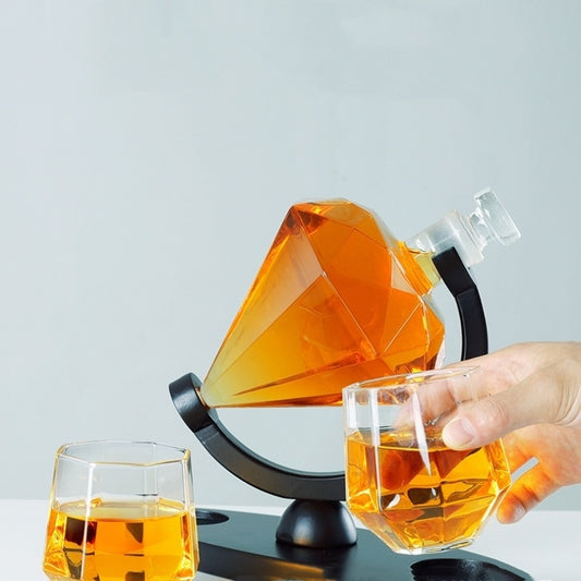 Diamond-shaped whiskey decanter with amber liquor on black stand and two faceted glasses