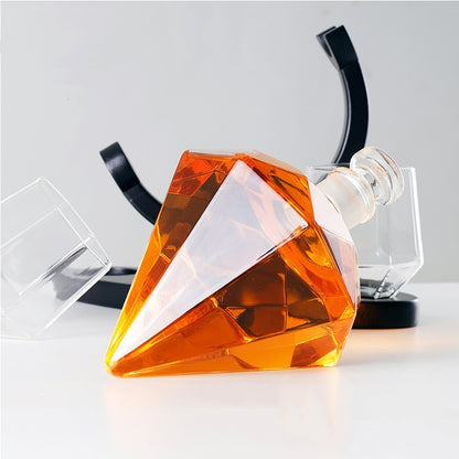 Diamond-shaped whiskey decanter with amber liquid, clear glass tumblers, and black stand on white surface