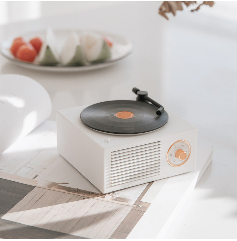 White retro mini phonograph Bluetooth speaker with black vinyl record on a white table in bright room