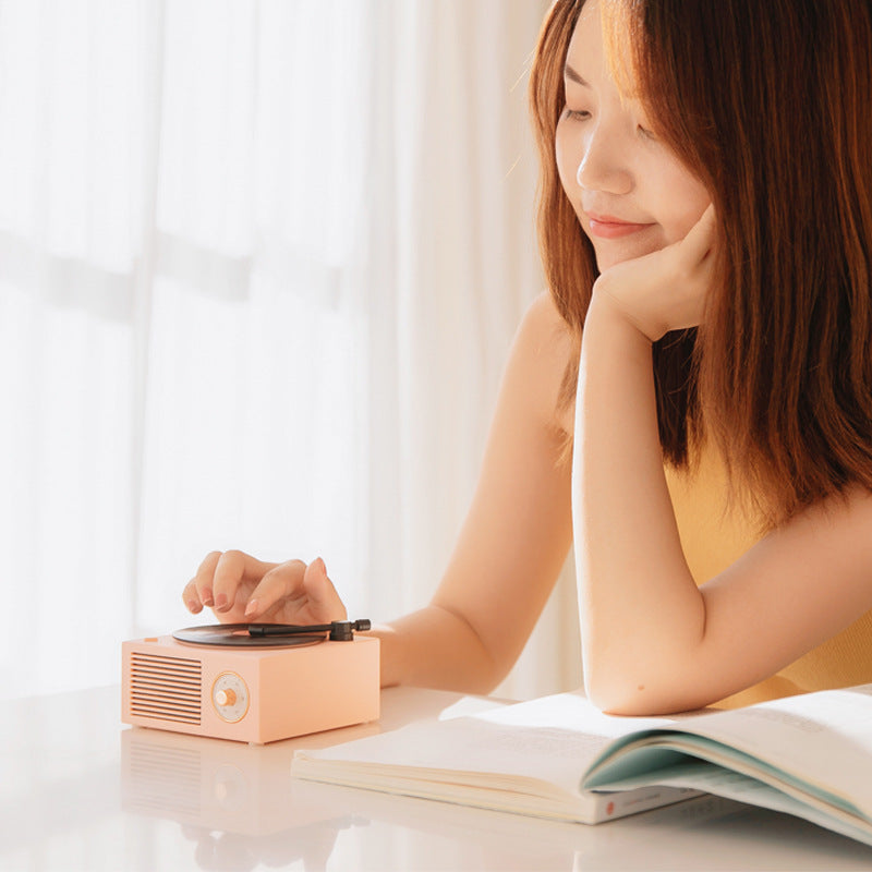 Young woman using Trendoligy retro mini phonograph Bluetooth speaker on white table with open book