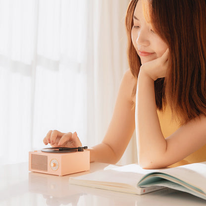 Young woman using Trendoligy retro mini phonograph Bluetooth speaker on white table with open book