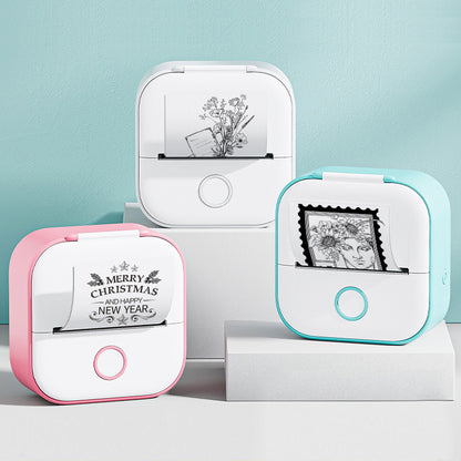 Three compact portable mini thermal printers in white with pink, white, and blue edges printing black and white images and text