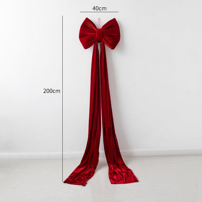 Large red velvet Christmas bow decoration with long trailing ribbons hanging on white wall