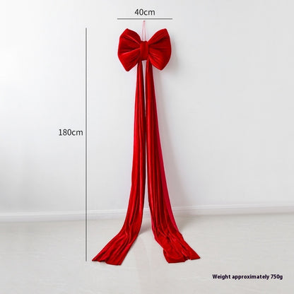 Large red velvet Christmas bow decoration with long flowing tails hanging on white wall