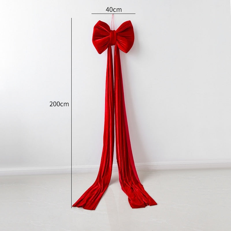 Large red velvet Christmas bow with long trailing ribbons hanging on white wall