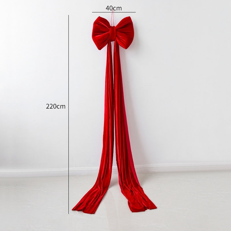 Large red velvet Christmas bow decoration with long tails hanging on white wall, 220cm by 40cm