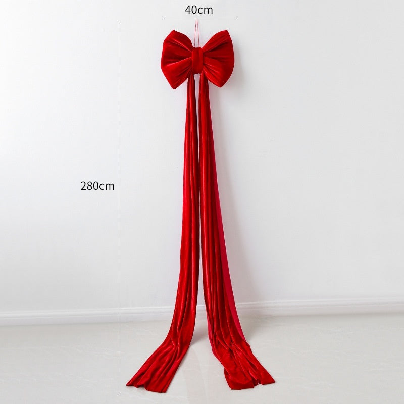 Large red velvet Christmas bow decoration with long trailing ribbons hanging on white wall