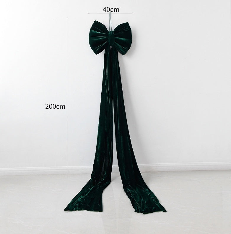 large dark green velvet bow with long tails hanging on white wall measuring 200cm by 40cm