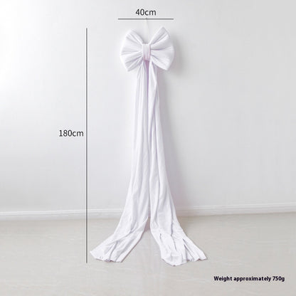 Large white fabric bow decoration with 40cm width and 180cm long tails hanging on white wall