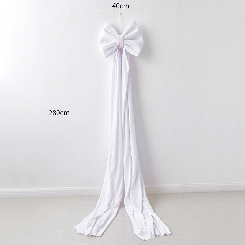 Large white fabric bow with long flowing tails, 40cm wide and 280cm length, against plain wall