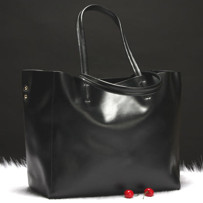 Glossy black leather tote bag with double handles on white fur with two cherries