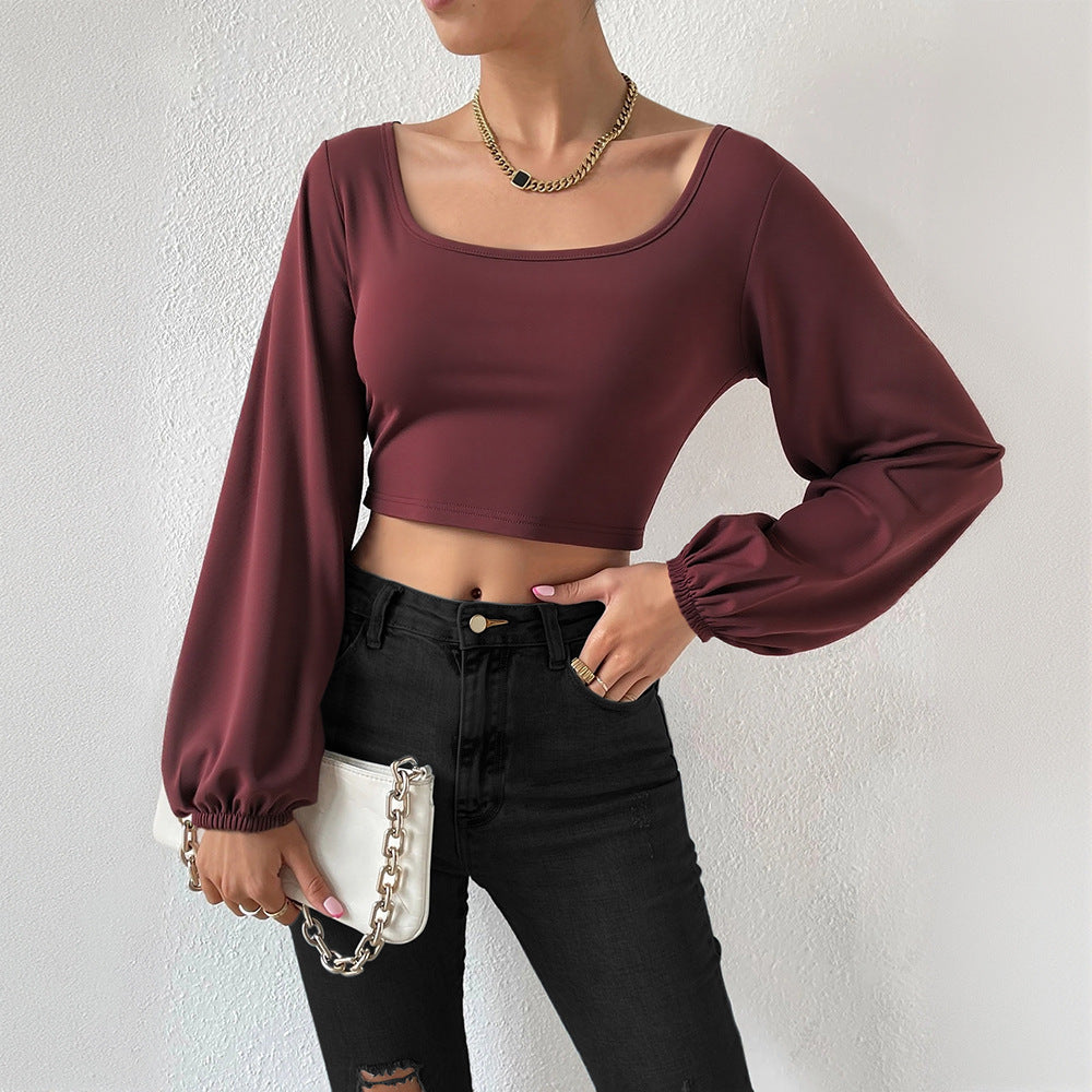 Woman wearing wine red lantern sleeve slim fit crop top with black high-waist jeans and white purse