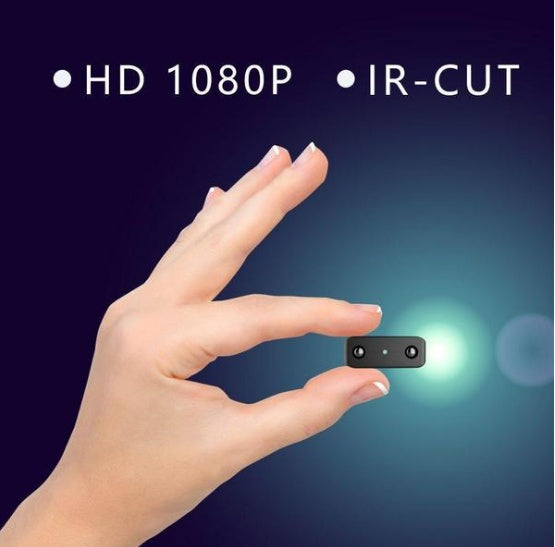 Hand holding a tiny black mini camera with HD 1080P and IR-CUT features on a dark blue background