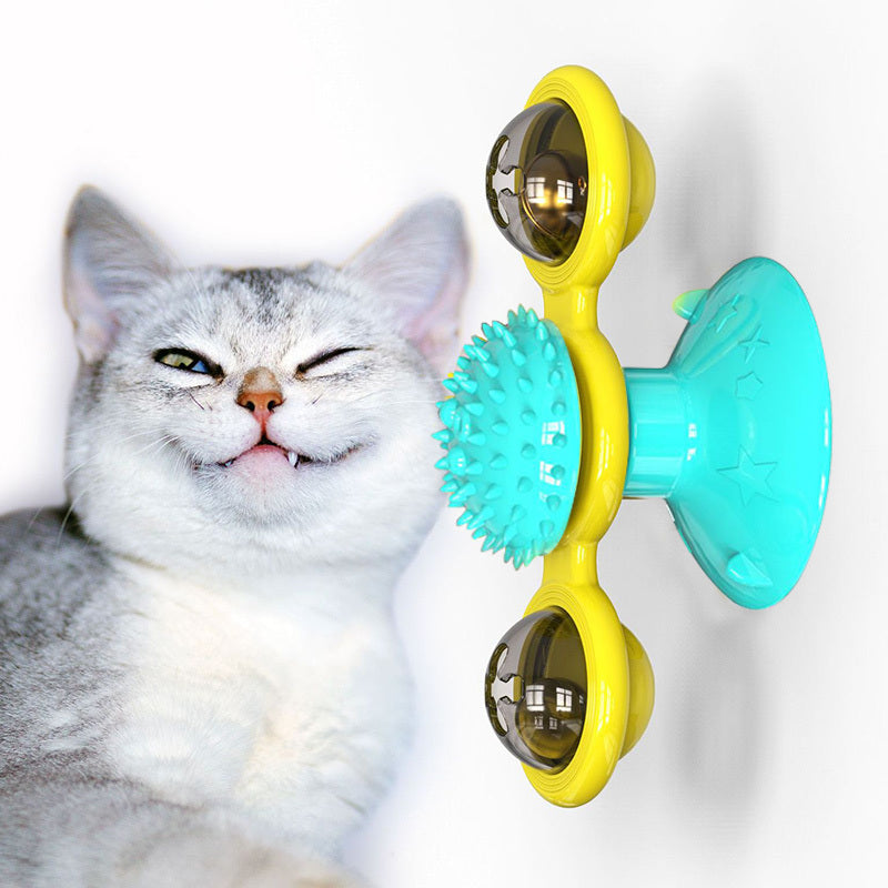 Gray and white cat winking next to a yellow and blue rotating suction cup cat toy with bells and spikes