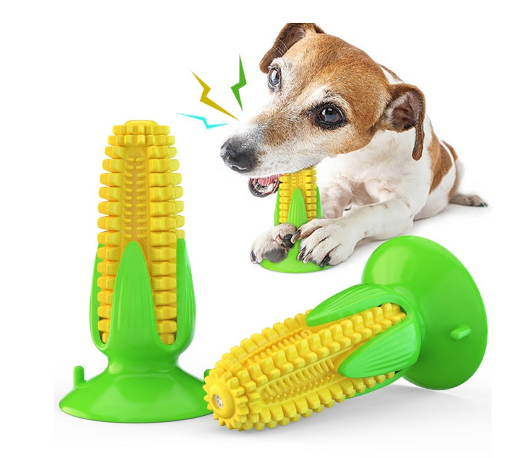 Durable yellow corn-shaped dog chew toy with green base, being chewed by a small brown and white dog
