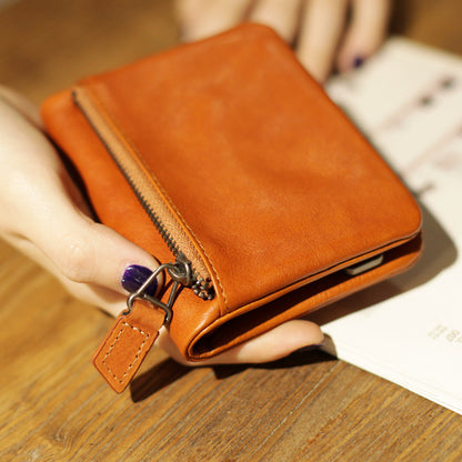 Hand holding a compact brown leather wallet with zipper detail on wooden table