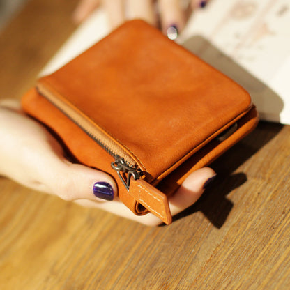 Hand holding a tan leather bifold wallet with zipper on wooden table