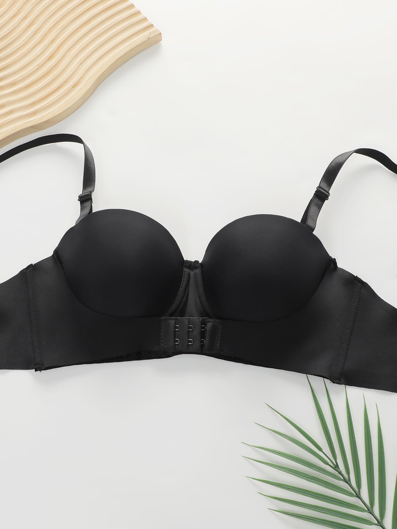 Black women's push-up bra with adjustable straps laid flat on white background with wooden and palm leaf accents