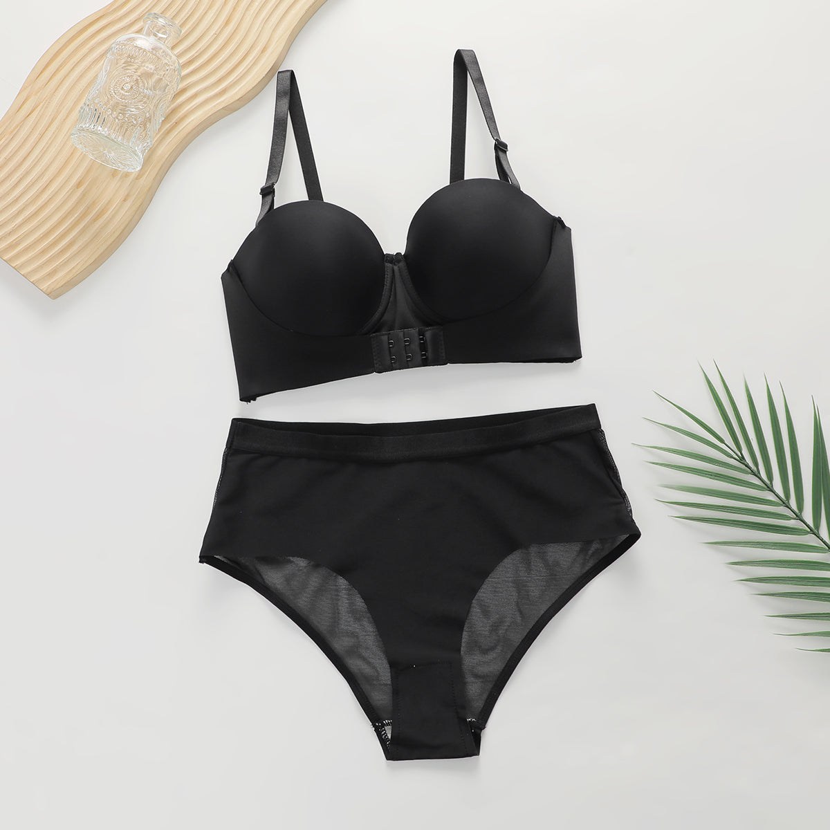 Black women's push-up bra and high-waisted panties lingerie set on white background with decorative leaf and glass bottle