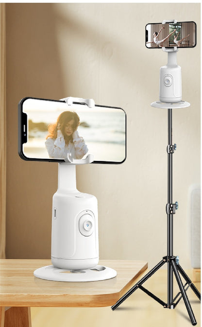 White AI smart gimbal phone holder on wooden table and tripod, holding phones showing a woman and a ballerina