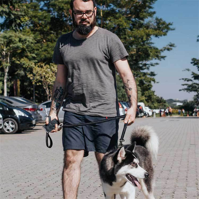 Man walking a black and white husky dog using a black adjustable bungee leash in a sunny outdoor parking lot