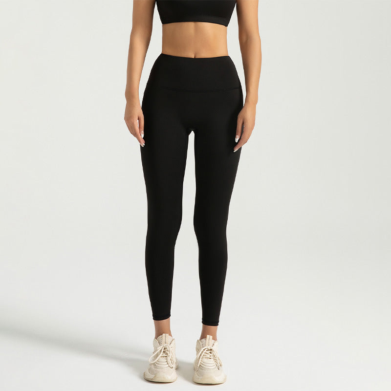 Woman wearing black high-waist leggings and black sports bra with white sneakers on plain background