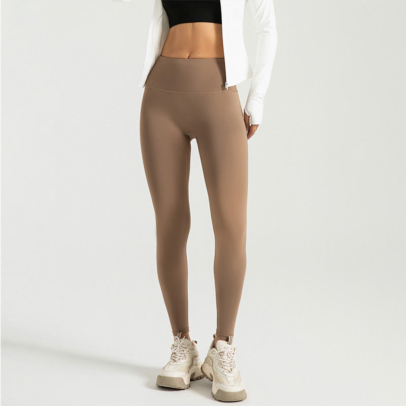 Woman wearing high-waist tan leggings with tummy control and white sneakers on plain background