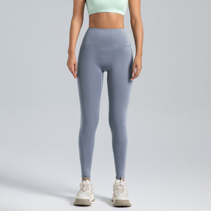 woman wearing high-waist grey leggings and a light green sports bra with white athletic shoes on grey background