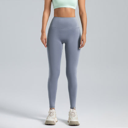 woman wearing high-waist grey leggings and a light green sports bra with white athletic shoes on grey background