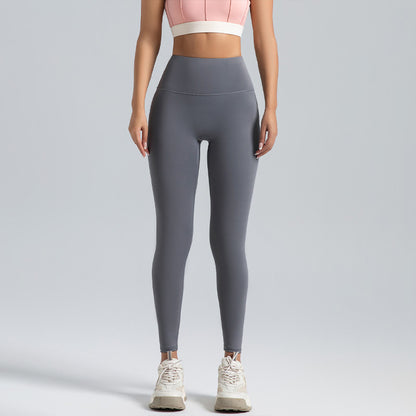 Woman wearing high-waist gray leggings and pink crop top, standing on plain gray background
