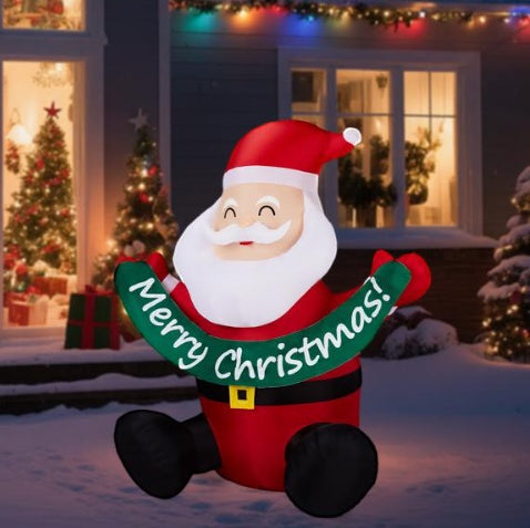 Inflatable Santa Claus decoration holding Merry Christmas banner, sitting outside a house with Christmas lights and snow