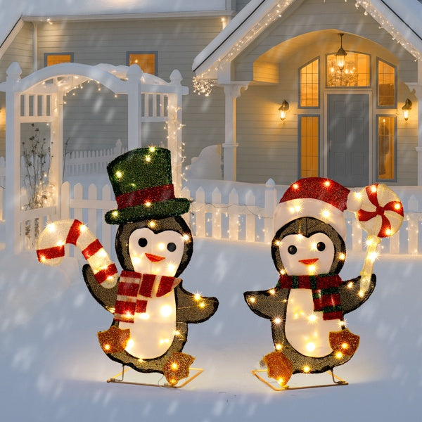 Two illuminated penguin Christmas decorations with scarves, candy cane, and peppermint in snowy yard