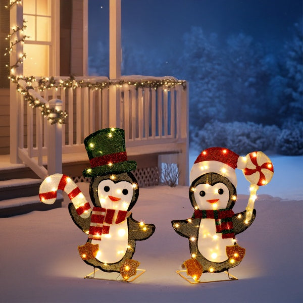 Two illuminated Christmas penguin decorations with scarves and hats holding candy canes outside snowy porch
