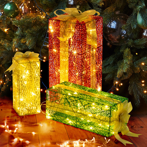 Set of three lighted decorative gift boxes in red, yellow, and green under Christmas tree with warm white LED lights