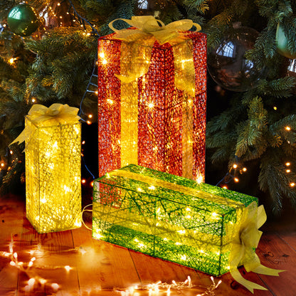 Set of three lighted decorative gift boxes in red, yellow, and green under Christmas tree with warm white LED lights