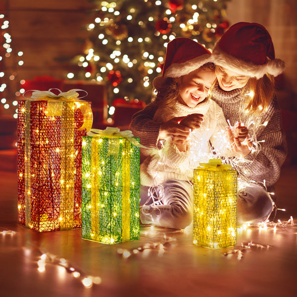 Mother and daughter in Santa hats with warm white LED lighted gift boxes by Christmas tree