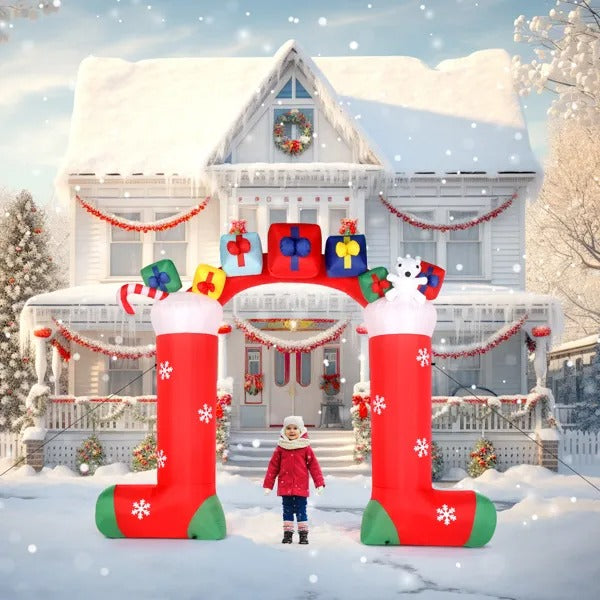 Child standing under large inflatable Christmas stocking arch with gifts and snowflakes in front of snow-covered house